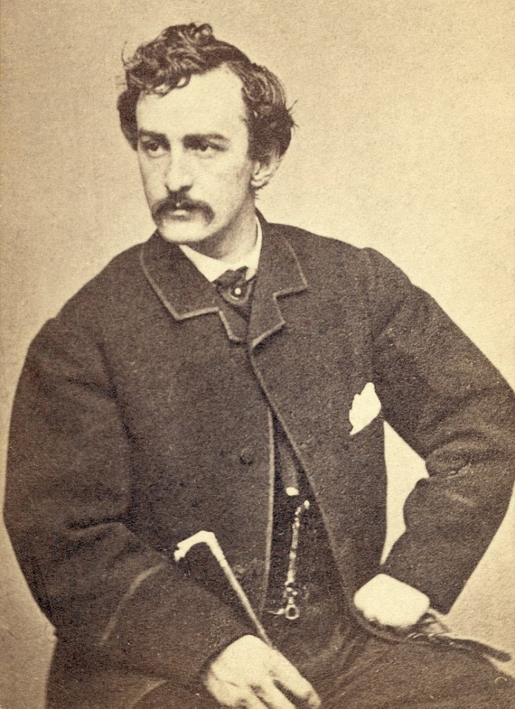 Sepia portrait of John Wilkes Booth, seated and looking away from camera.